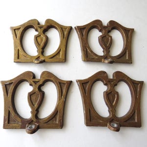 May include: Four antique bronze-colored drawer pulls. Each pull features a decorative design with an open heart shape and a central shield-like element. The pulls have a small, circular opening for a screw.