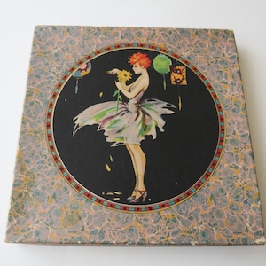 Könnte beinhalten: Quadratische Schachtel mit einer Vintage-Illustration einer Frau in einem fließenden Kleid, die eine Blume hält, vor einem schwarzen Hintergrund. Die Illustration wird von einem kreisförmigen Rahmen umgeben und von einem Marmormuster umgeben.