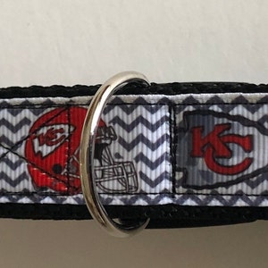 May include: A black and white chevron patterned dog collar with a red and white Kansas City Chiefs logo. The collar has a black plastic buckle.