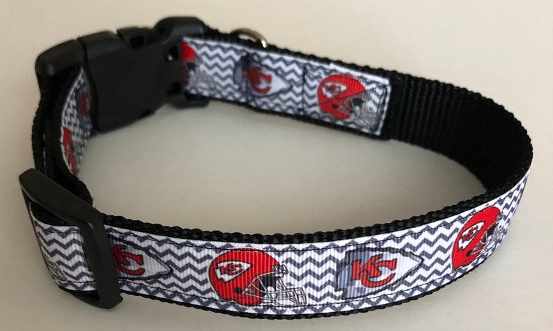 May include: A black dog collar with a white and gray chevron pattern and red and white Kansas City Chiefs logos.
