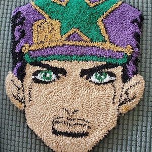 May include: A close-up of a hand-crafted rug depicting a cartoon character with a purple hat, green hair, and a serious expression. The rug is made of looped yarn in shades of purple, green, brown, and black.