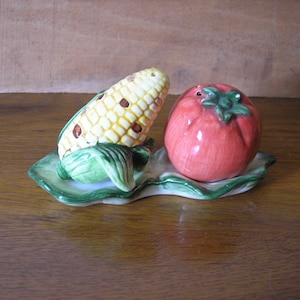 Può includere: Un set di saliera e pepe in ceramica a forma di pannocchia di mais e pomodoro, su un vassoio verde a forma di foglia.