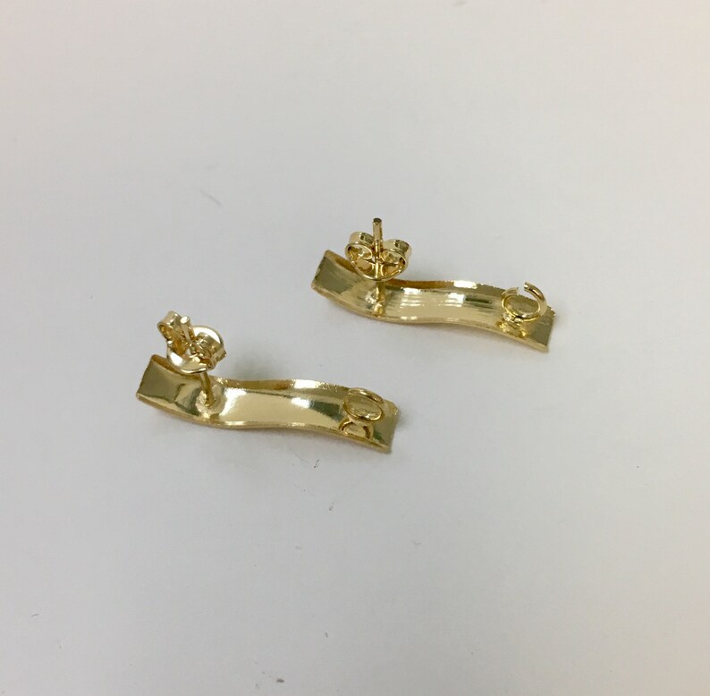 Peut inclure: Une paire de boucles d'oreilles dor&eacute;es avec un design incurv&eacute; en forme de vague. Les boucles d'oreilles sont en m&eacute;tal et ont un fermoir &agrave; tige.