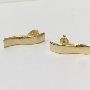 Peut inclure: Une paire de boucles d'oreilles dor&eacute;es avec une finition ondul&eacute;e bross&eacute;e. Les boucles d'oreilles sont en m&eacute;tal et ont un fermoir &agrave; tige.