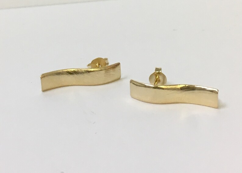 Peut inclure: Une paire de boucles d'oreilles dor&eacute;es avec une finition ondul&eacute;e bross&eacute;e. Les boucles d'oreilles sont en m&eacute;tal et ont un fermoir &agrave; tige.