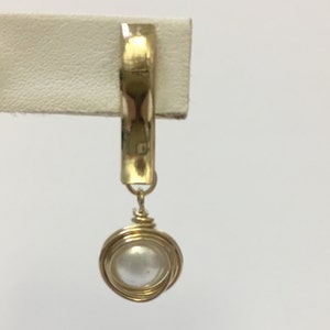 Peut inclure: Une boucle d'oreille en fil d'or avec un pendentif en perle blanche.