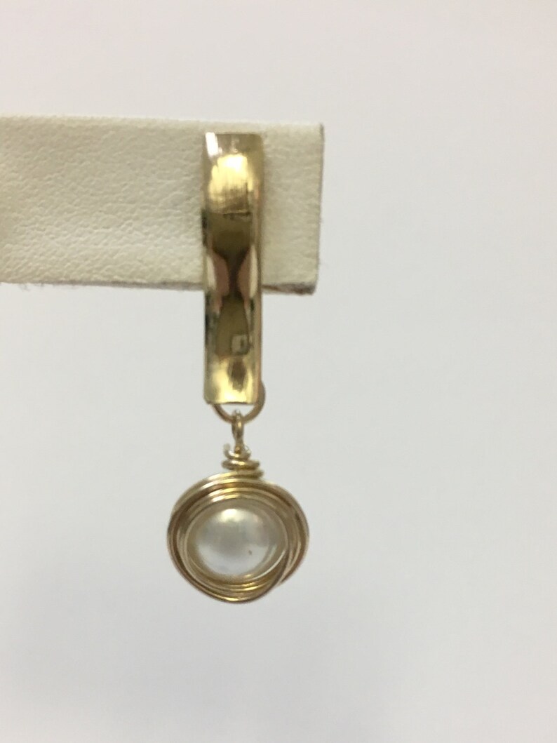 Peut inclure: Une boucle d'oreille en fil d'or avec un pendentif en perle blanche.