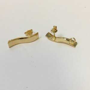 Peut inclure: Une paire de boucles d'oreilles dor&eacute;es avec un design incurv&eacute; et ondul&eacute;. Les boucles d'oreilles sont en m&eacute;tal et ont une fermeture &agrave; tige.