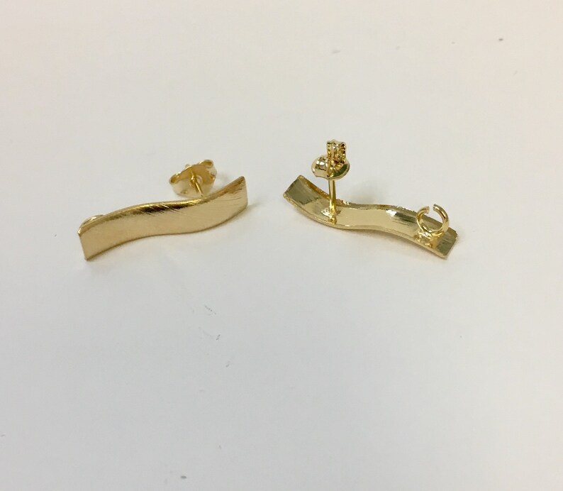 Peut inclure: Une paire de boucles d'oreilles dor&eacute;es avec un design incurv&eacute; et ondul&eacute;. Les boucles d'oreilles sont en m&eacute;tal et ont une fermeture &agrave; tige.