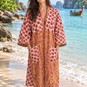 May include: A knee-length open-front robe featuring a patchwork design with alternating panels of red and white circular patterns and a dense gold and red floral print, complete with two large front patch pockets and wide sleeves.
