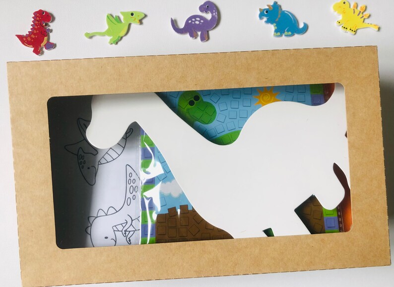 May include: A brown cardboard box with a cutout in the shape of a dinosaur. The cutout reveals a colorful dinosaur-themed design with a white dinosaur silhouette.