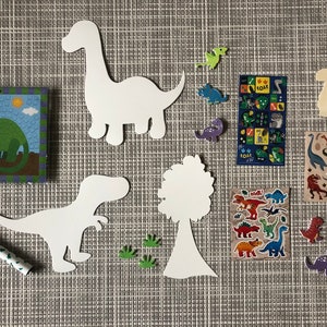 May include: A set of dinosaur-themed craft supplies for kids. The set includes white paper cutouts of dinosaurs, a tree, and footprints, a green marker, and a sheet of dinosaur stickers. The stickers feature colorful dinosaurs with the word "Roar!" printed on them.