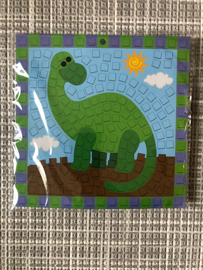 May include: A green dinosaur mosaic craft kit with a blue background, a yellow sun, and white clouds. The kit includes small, colorful squares to create the mosaic.