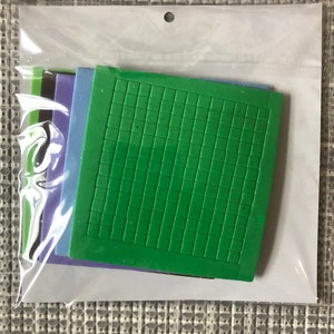 May include: A set of five foam stamps in a clear plastic bag. The stamps are in different colors: green, blue, purple, black, and green. The green stamp has a grid pattern.