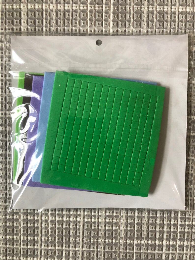 May include: A set of five foam stamps in a clear plastic bag. The stamps are in different colors: green, blue, purple, black, and green. The green stamp has a grid pattern.