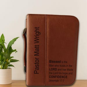 May include: A brown leather-like Bible cover with a side handle. The front is engraved with the text Pastor Matt Wright and the verse Blessed is the Man who trusts in the LORD and has Made the Lord his hope and CONFIDENCE Jeremiah 17:7.