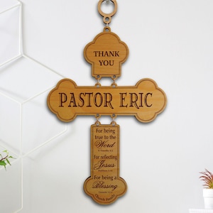 May include: A light brown wooden wall hanging shaped like a cross, featuring the engraved text THANK YOU, PASTOR ERIC, and a longer message including For being true to the Word, For reflecting Jesus, and For being a blessing from the Church Family.