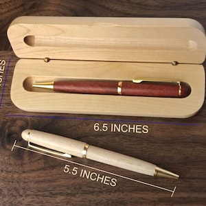 May include: A dark reddish-brown pen with gold accents resting inside an open light-colored wooden case, alongside a second light-colored wooden pen with gold accents. The case measures 6.5 inches by 2.0 inches, and the pen measures 5.5 inches.