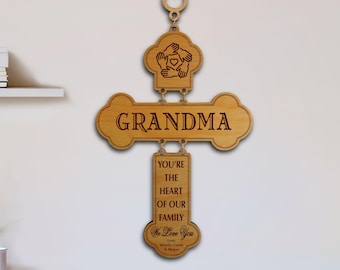 May include: A light brown wooden wall hanging composed of three connected pieces. The top piece features a circular design of hands around a heart. The middle piece reads GRANDMA. The bottom piece reads YOU'RE THE HEART OF OUR FAMILY We Love You Love, Wendy, Candy & Megan.