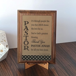 May include: A wooden framed plaque with a light brown background and the word "PASTOR" vertically on the left. The plaque has a message that reads "Thank You PASTOR JONAH for all you have done."
