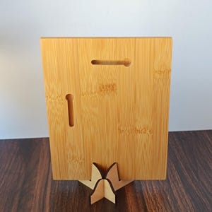 May include: A rectangular bamboo plaque with a keyhole slot and a vertical slot on the back. The plaque is supported by a wooden stand. The bamboo has a natural, light brown color and visible grain.