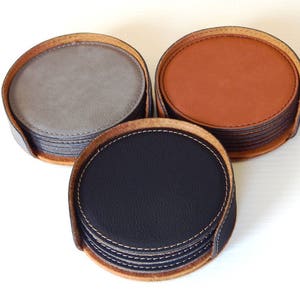 May include: Set of six leather coasters in gray, brown, and black. Each coaster has a stitched edge and is stacked on top of each other.