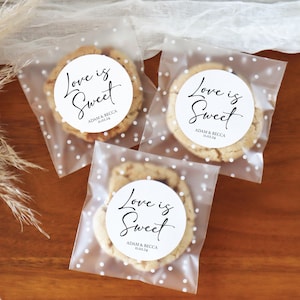 May include: Three clear cellophane bags with white polka dots, each containing a cookie with a round white sticker that says "Love is Sweet" with the couple's names and wedding date below.