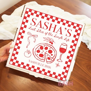 May include: A white pizza box with a red checkered border and red illustrations. The text "SASHA'S Last Slice of the Single Life" is displayed. Other illustrations include a pizza, wine glass, and tomato. The text "NASHVILLE 2026" is also present.