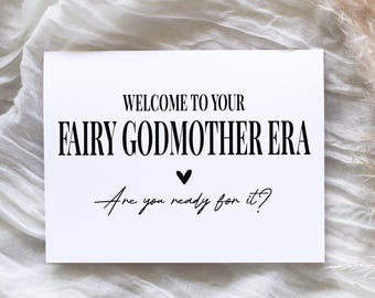 May include: A white rectangular greeting card featuring black text that reads: WELCOME TO YOUR FAIRY GODMOTHER ERA, followed by a small black heart icon and the script text: Are you ready for it? The card has a clean, minimalist design.
