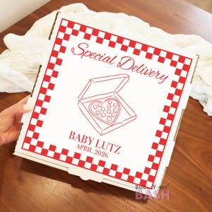 May include: A white pizza box with a red checkered border and the words "Special Delivery" in a script font. Inside the box is a heart-shaped pizza. The text "BABY LUTZ APRIL 2026" is also printed on the box.