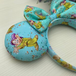 May include: Light blue headband with a large bow and a pattern of a cartoon character. The headband is decorated with glitter.