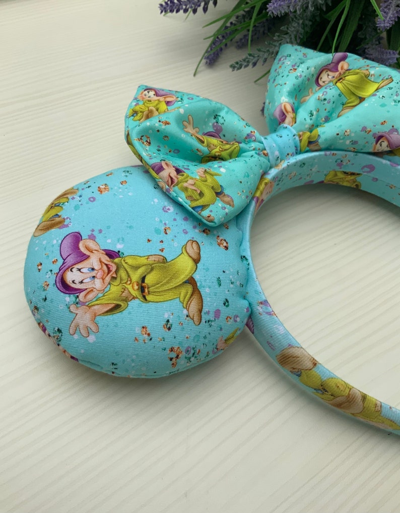 May include: Light blue headband with a large bow and a pattern of a cartoon character. The headband is decorated with glitter.