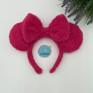 May include: Pink fluffy headband with a large bow and ears. The headband has a tag that says "Handmade Ah Antikapr".