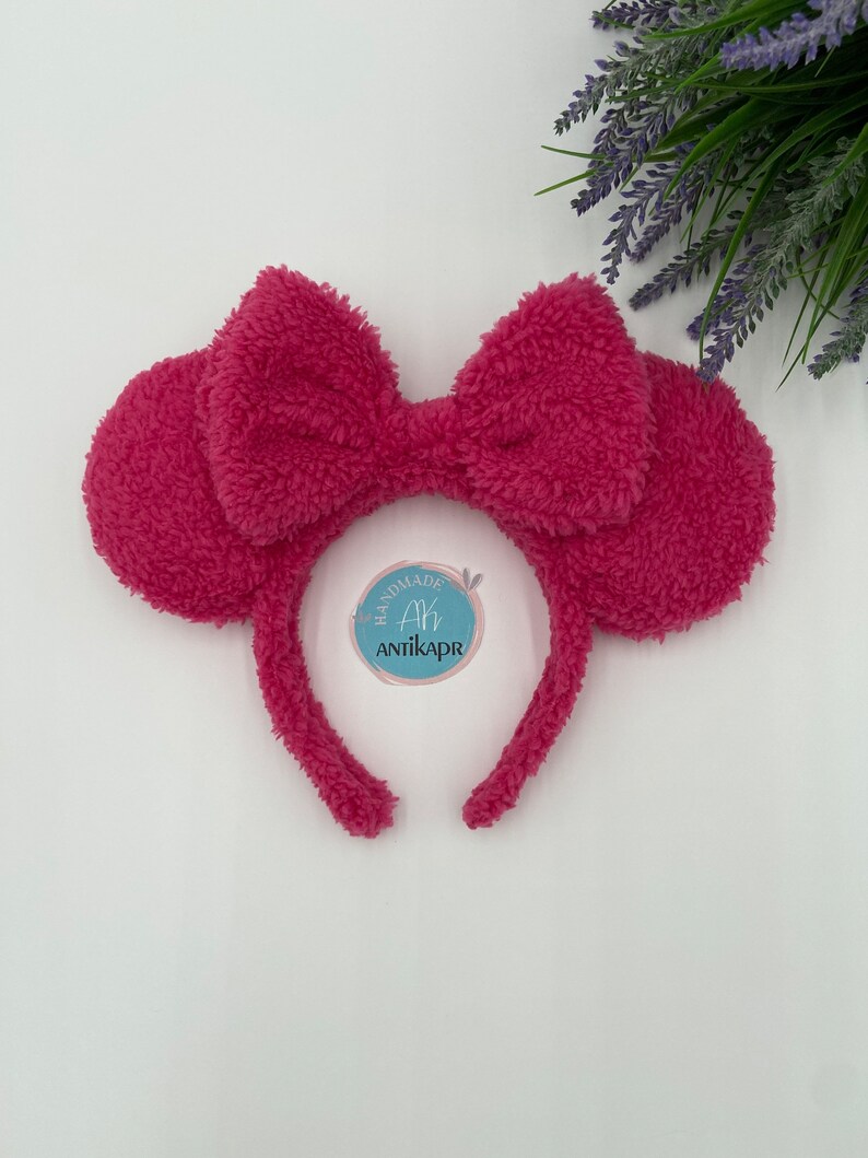 May include: Pink fluffy headband with a large bow and ears. The headband has a tag that says "Handmade Ah Antikapr".