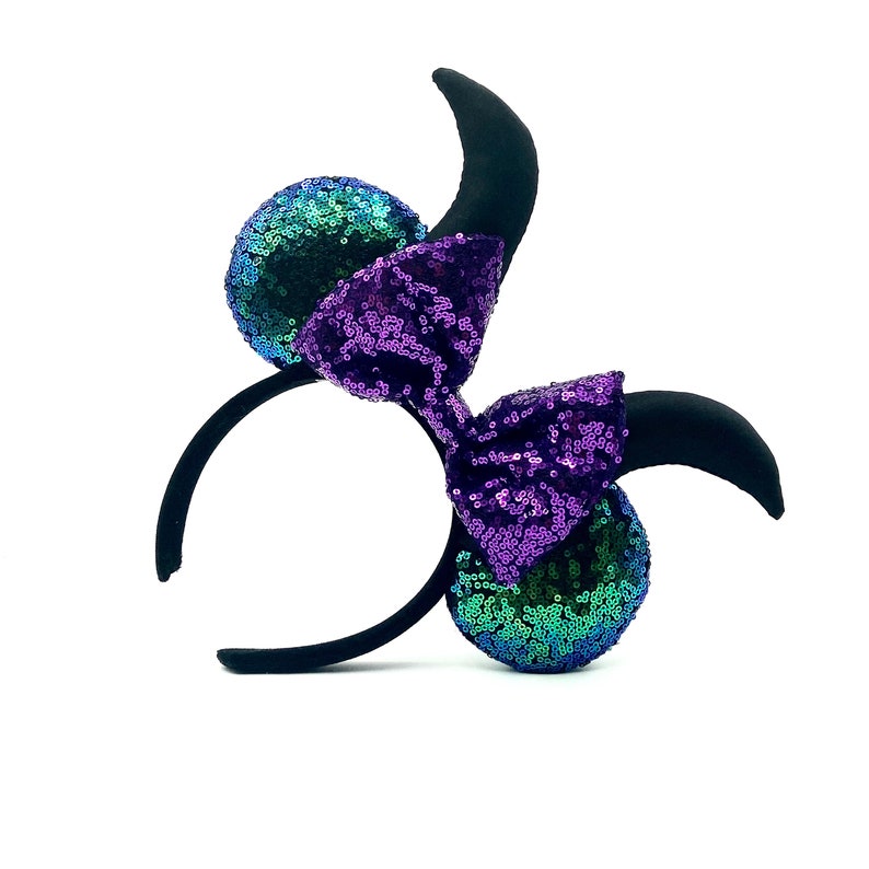 Op de afbeelding: Een zwart hoofdband met paarse en groene pailletten oren en een grote paarse strik. De oren zijn gevormd als Mickey Mouse oren.