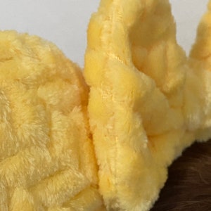 May include: A pair of yellow plush ear warmers with a waffle-like texture. The ear warmers are made of soft, fuzzy fabric.