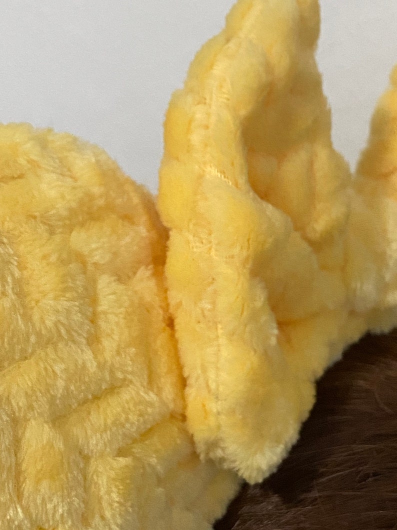 May include: A pair of yellow plush ear warmers with a waffle-like texture. The ear warmers are made of soft, fuzzy fabric.