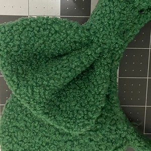 K&ouml;nnte beinhalten: Ein gr&uuml;nes, flauschiges Stirnband mit einer geknoteten Schleife. Das Stirnband ist aus einem weichen, pl&uuml;schigen Material.