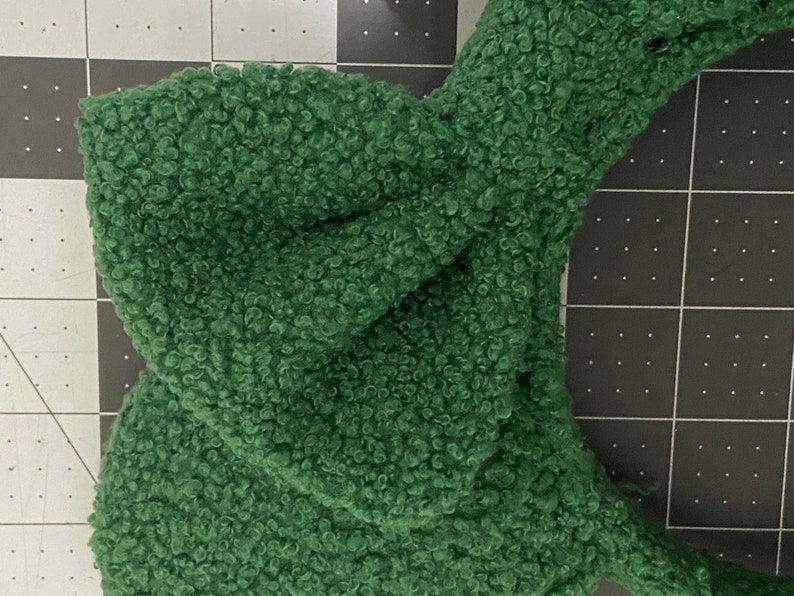 K&ouml;nnte beinhalten: Ein gr&uuml;nes, flauschiges Stirnband mit einer geknoteten Schleife. Das Stirnband ist aus einem weichen, pl&uuml;schigen Material.
