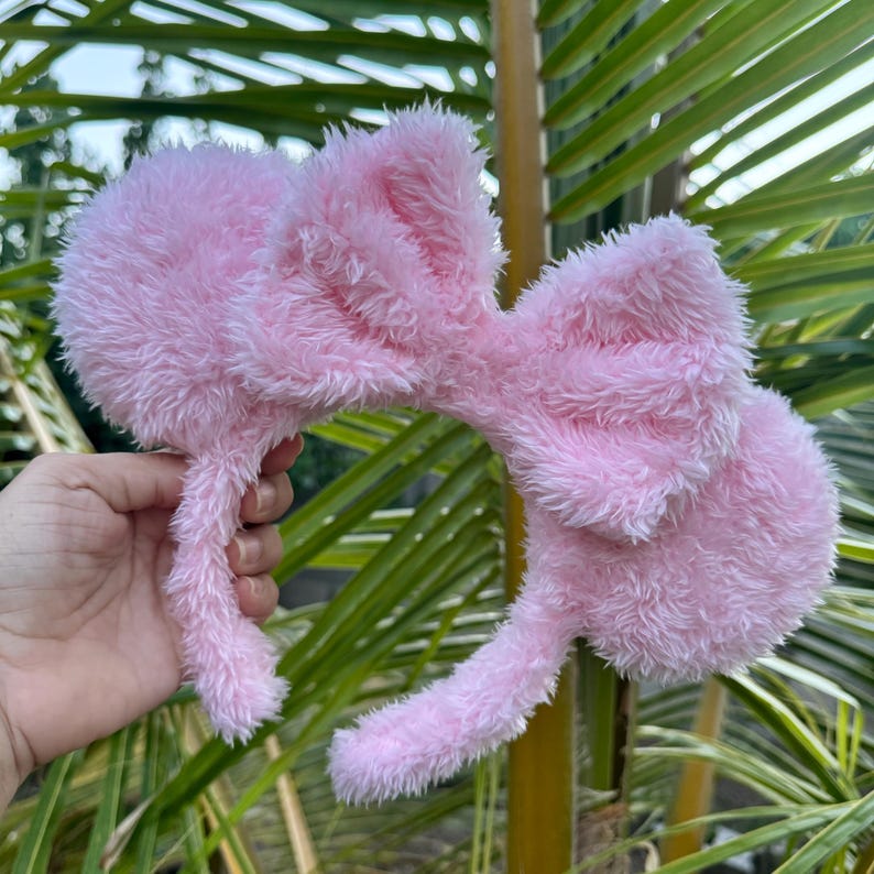 Op de afbeelding: Roze pluche Minnie Mouse oren haarband met een grote strik. De haarband is gemaakt van zacht, pluche materiaal.