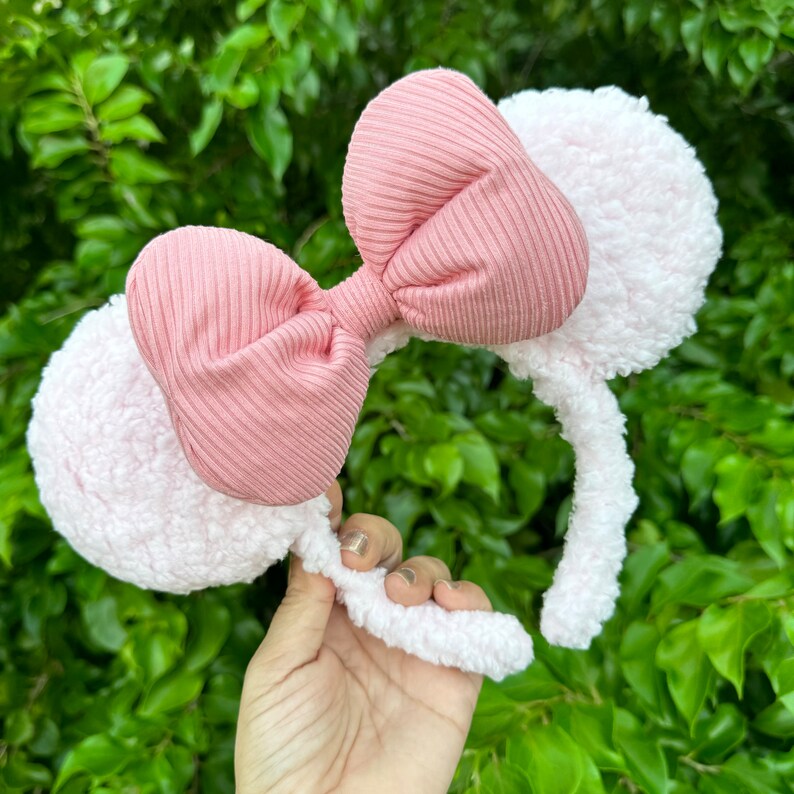 Pode incluir: Faixa de cabe&ccedil;a felpuda rosa e branca com um la&ccedil;o rosa. A faixa de cabe&ccedil;a &eacute; feita de um material macio e felpudo e tem um la&ccedil;o rosa no topo.