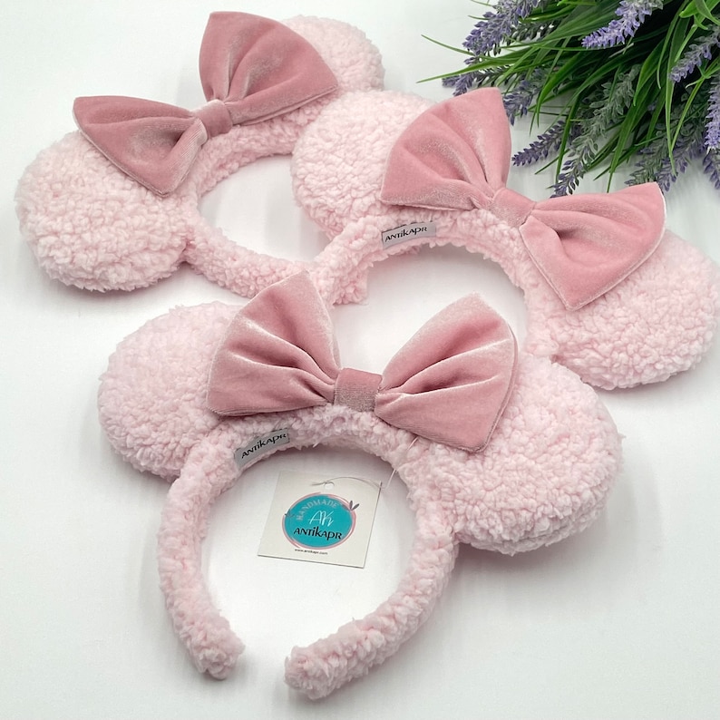 May include: Two pink fuzzy headbands with pink velvet bows. The headband is decorated with a small white tag that says "Antikapris".