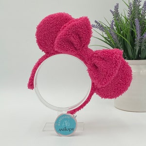 May include: A pink fluffy headband with a large bow. The headband is on a white stand with a blue circle label that says "Handmade Ah Antikapr".