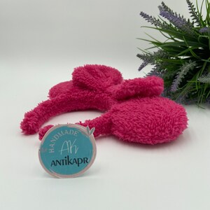 May include: Pink fluffy headband with bunny ears. The headband has a sticker that says "Handmade Ak Antikapr".
