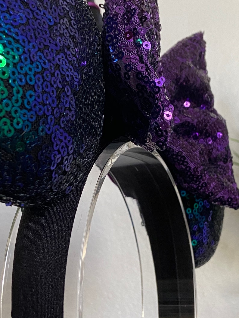 Op de afbeelding: Paarse en groene Minnie Mouse oren met pailletten en een zwart hoofdband. De strik is gemaakt van paarse pailletten en heeft een gelaagd ontwerp.
