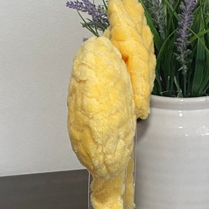 May include: Two yellow plush headbands with a fuzzy texture. The headbands are on a clear display stand.
