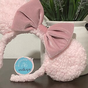May include: Pink fuzzy mouse ears headband with a large pink velvet bow. The headband has a small blue circle tag with the text "Handmade Ah Antikapr".