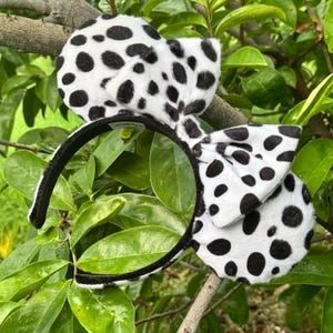May include: Black and white dalmatian print headband with a large bow. The headband is made of soft, fuzzy fabric.