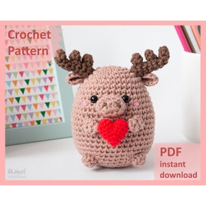 May include: Crochet pattern for a brown amigurumi reindeer holding a red heart. The pattern is available as an instant PDF download.