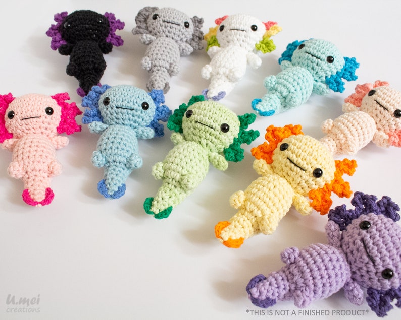 May include: A collection of 10 crocheted axolotl plushies in various colours, including pink, blue, green, yellow, orange, purple, white, grey, and black. Each axolotl has a unique colour combination and features a cute, smiling face.